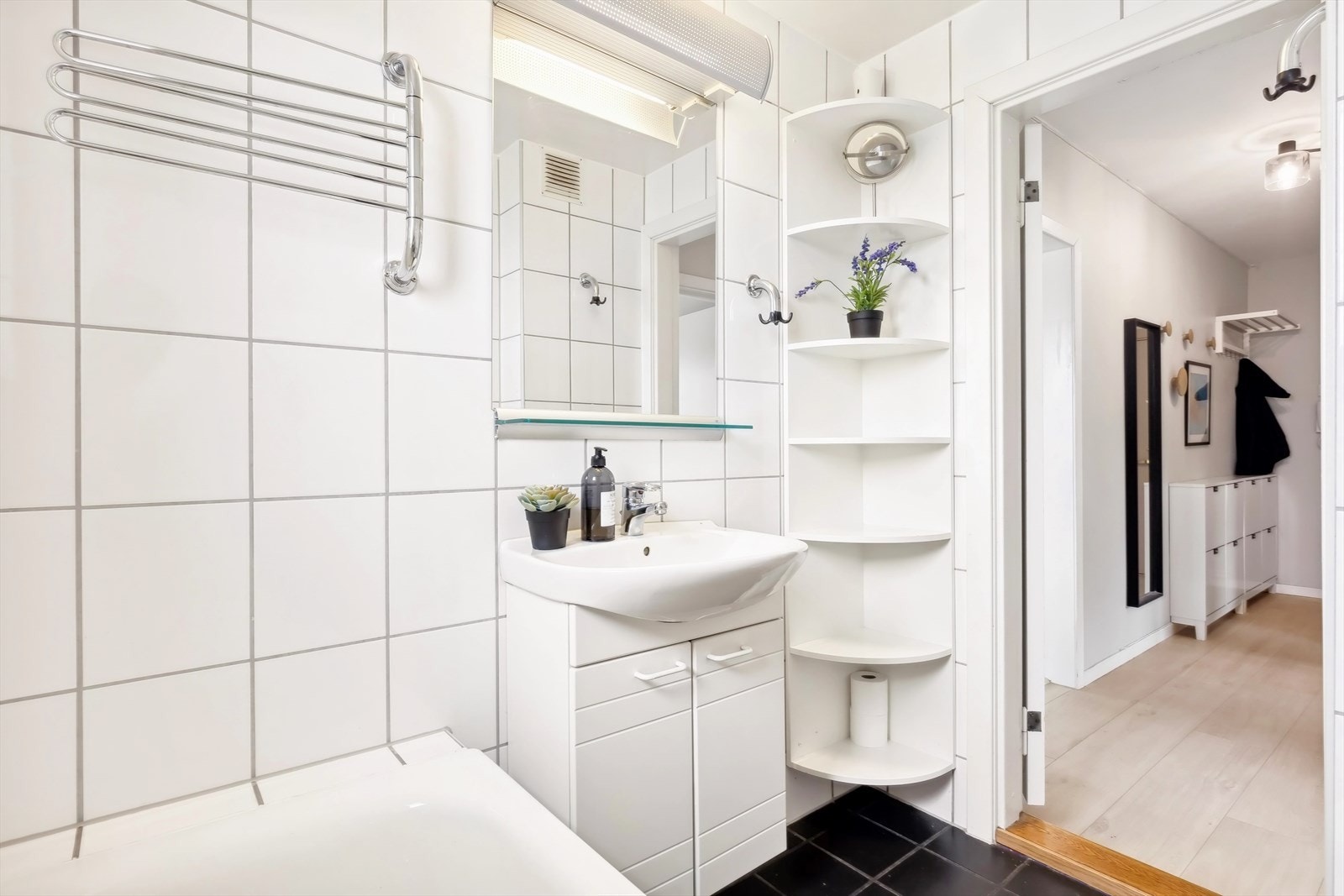 Badet inneholder baderomsinnredning med malte fronter, heldekkende servant, toalett, speil med overliggende belysning, vegghyller og badekar med dusjbatteri. Galleribilde