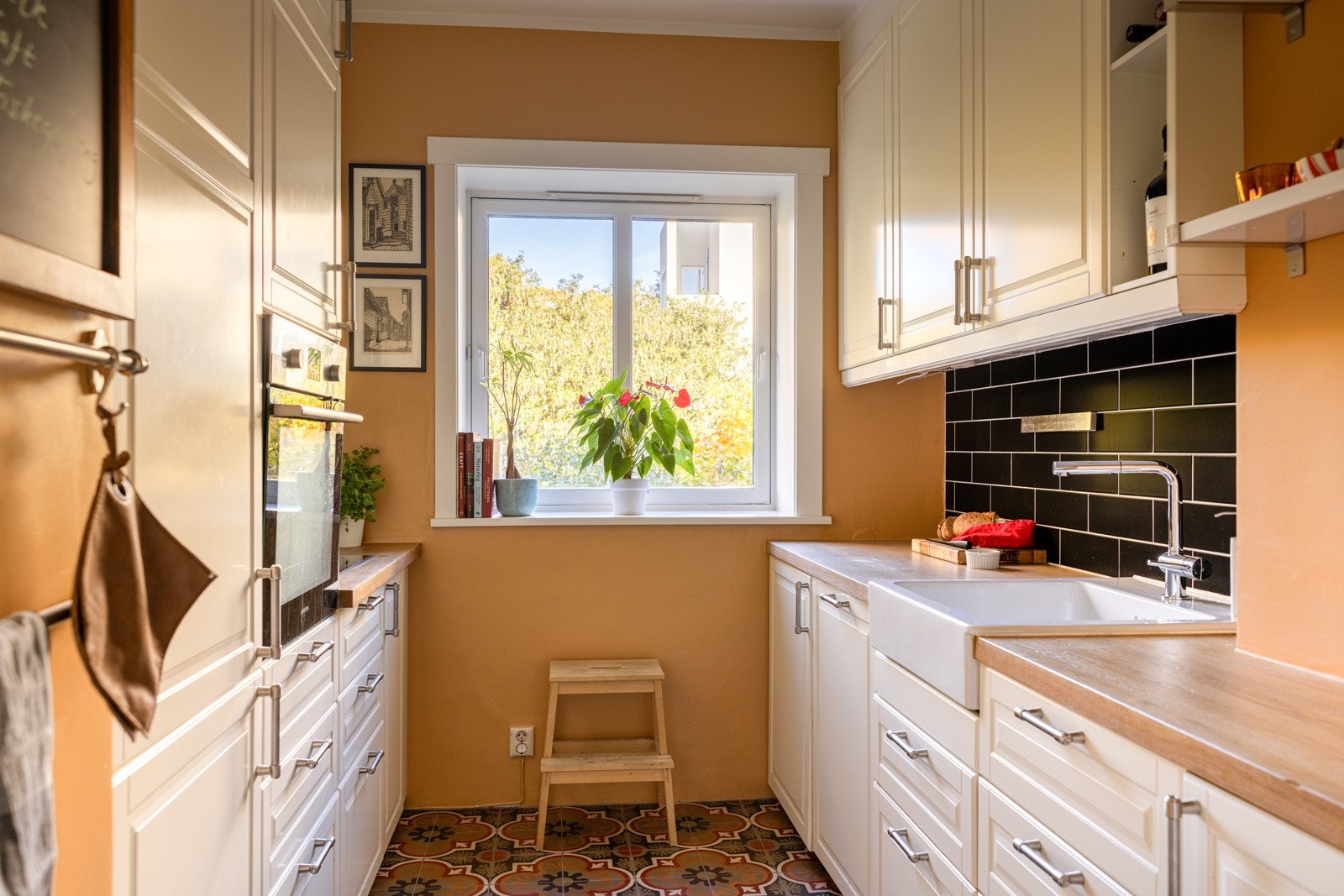 Kjøkkenet fremstår lyst og moderne, med stilrene profilerte fronter og en flott benkeplate i treverk som tilfører en naturlig varme til rommet. Gulvet er dekorativt flislagt i et mønster som skaper en herlig kontrast til de ellers lyse innredningene. Galleribilde