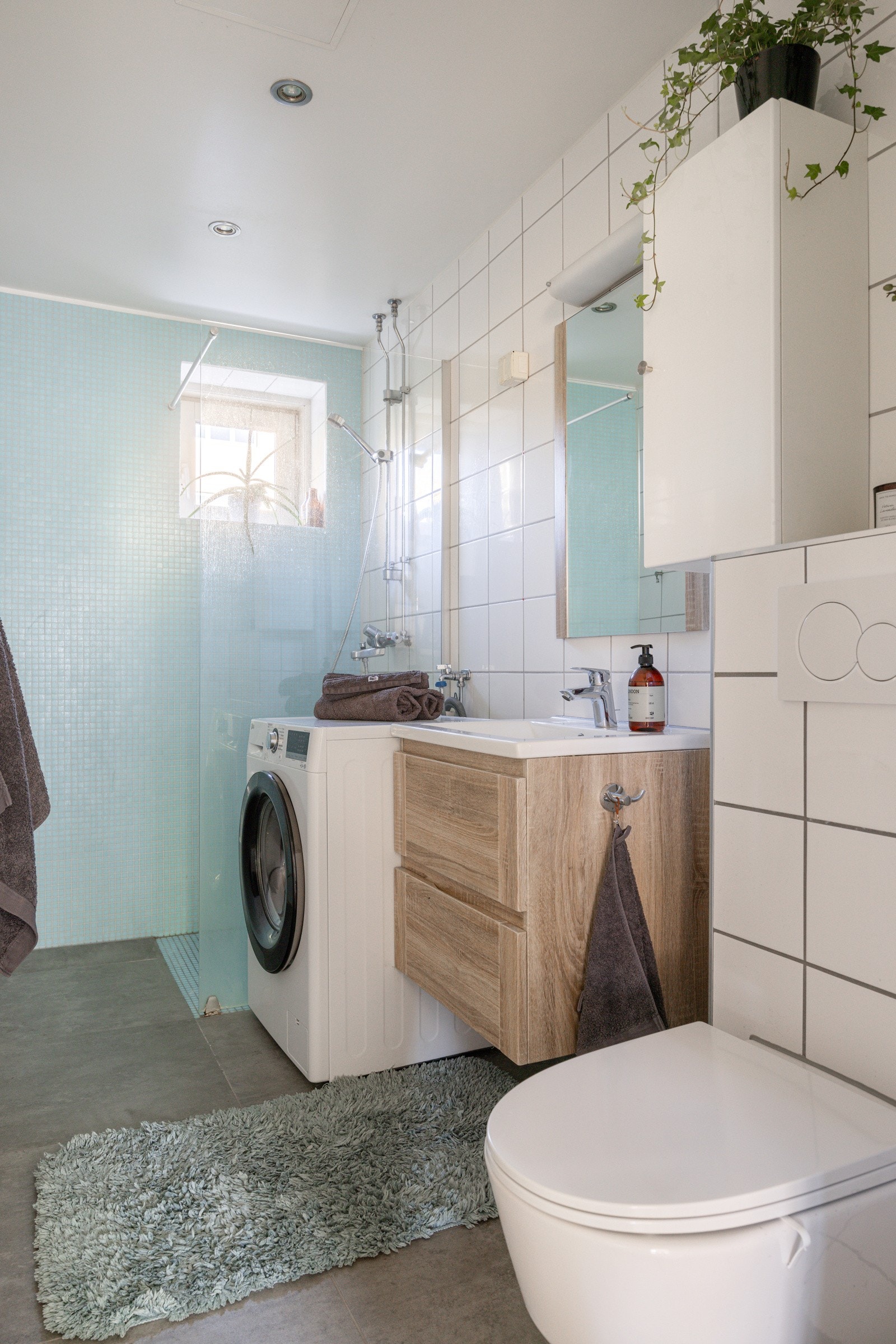 Dusjsonen er elegant adskilt med en glassvegg, og veggene er kledd med stilfulle mosaikkfliser i dusjområdet. Badet har en vegghengt servantinnredning med skuffer som gir godt med oppbevaringsplass, og over servanten henger et speil med praktisk belysning Galleribilde