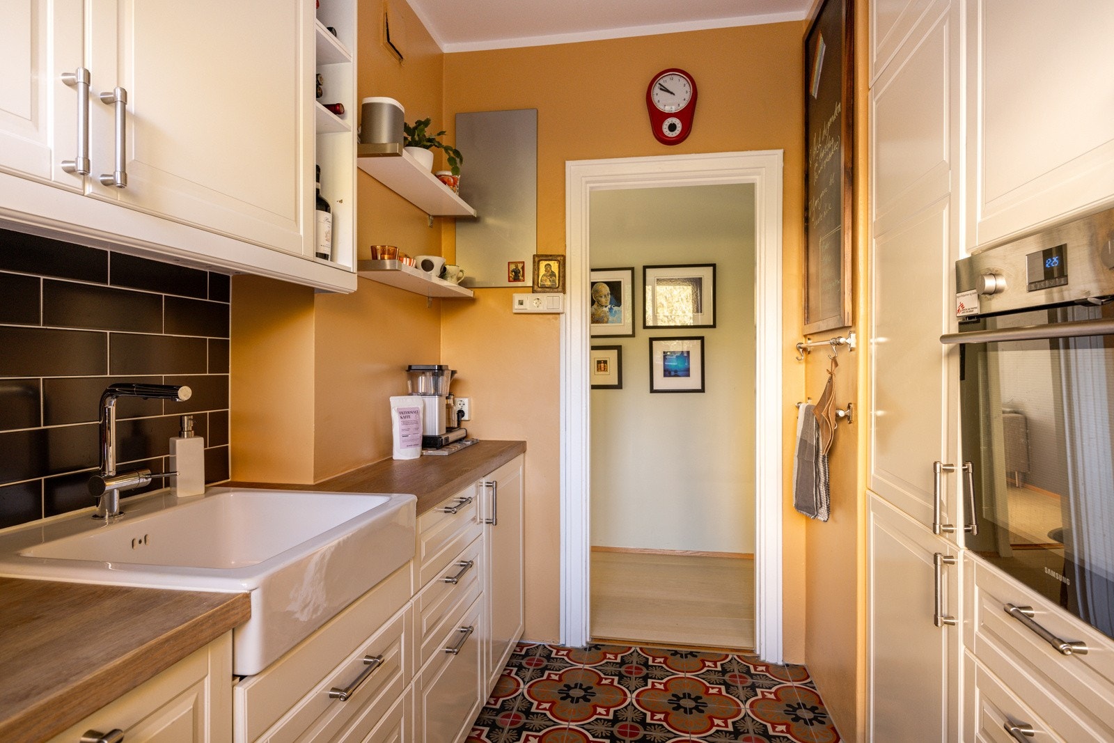 Mellom overskapene og benkeplaten er det satt opp elegante, svarte fliser som gir kjøkkenet et moderne og tidløst preg. Kjøkkenet er utstyrt med takhøye overskap som gir ekstra oppbevaringsplass og utnytter høyden i rommet på en smart måte. Galleribilde