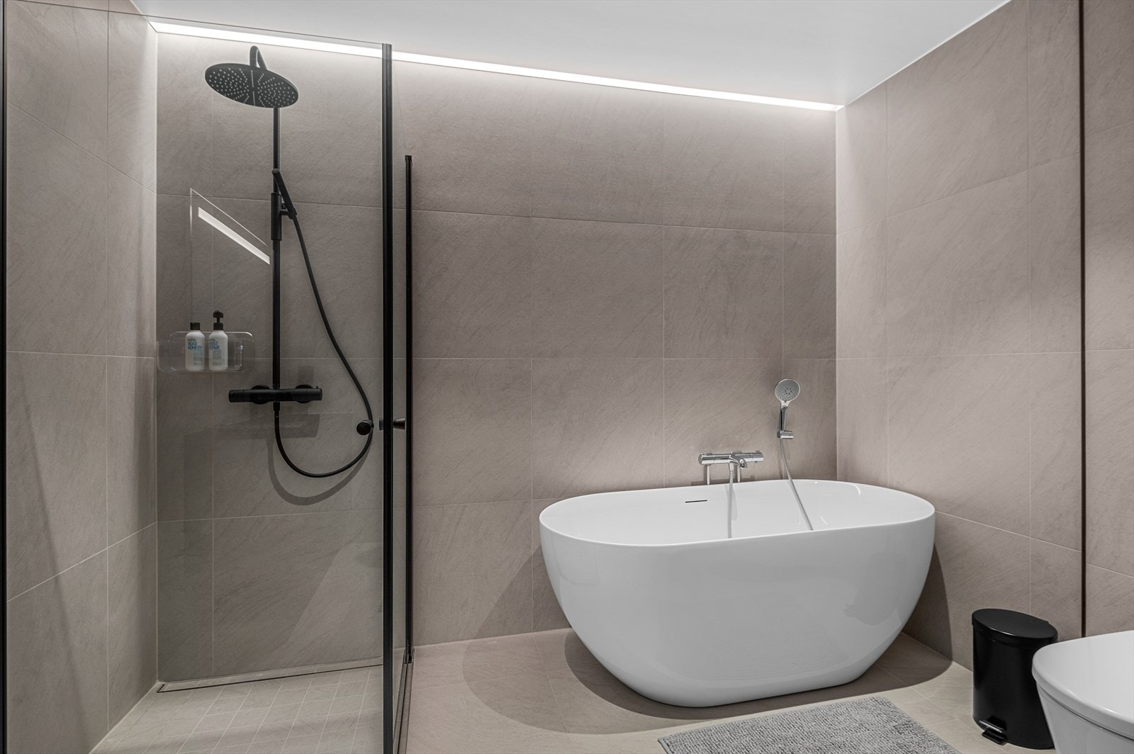 Badet er innredet med dusjhjørne med innfellbare glassdører, badekar og dusjgarnityr, veggmontert toalett og servantskap, speil med integrert lys over servant. I tillegg får du en lekker lysstripe over dusjsone Galleribilde