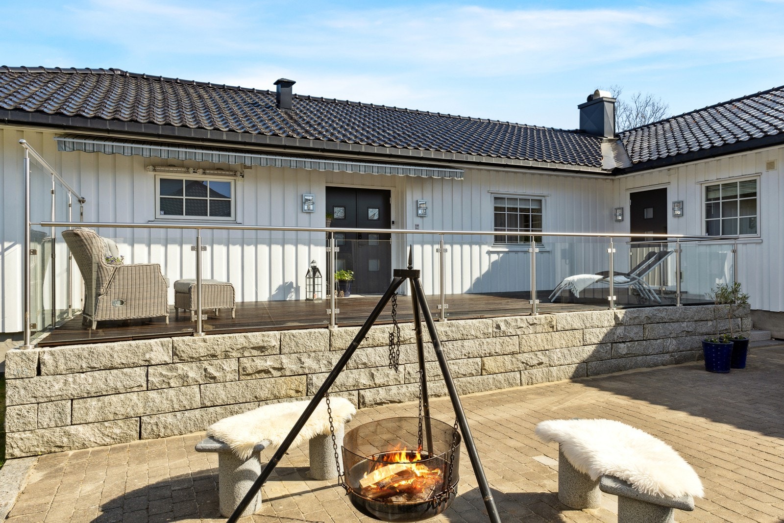 Vestvendt terrasse ved inngangsparti er oppført med naturstein i ringmur, gulv med terrassebord samt stål og glass i rekkverk. Enkel trapp i naturstein. Galleribilde