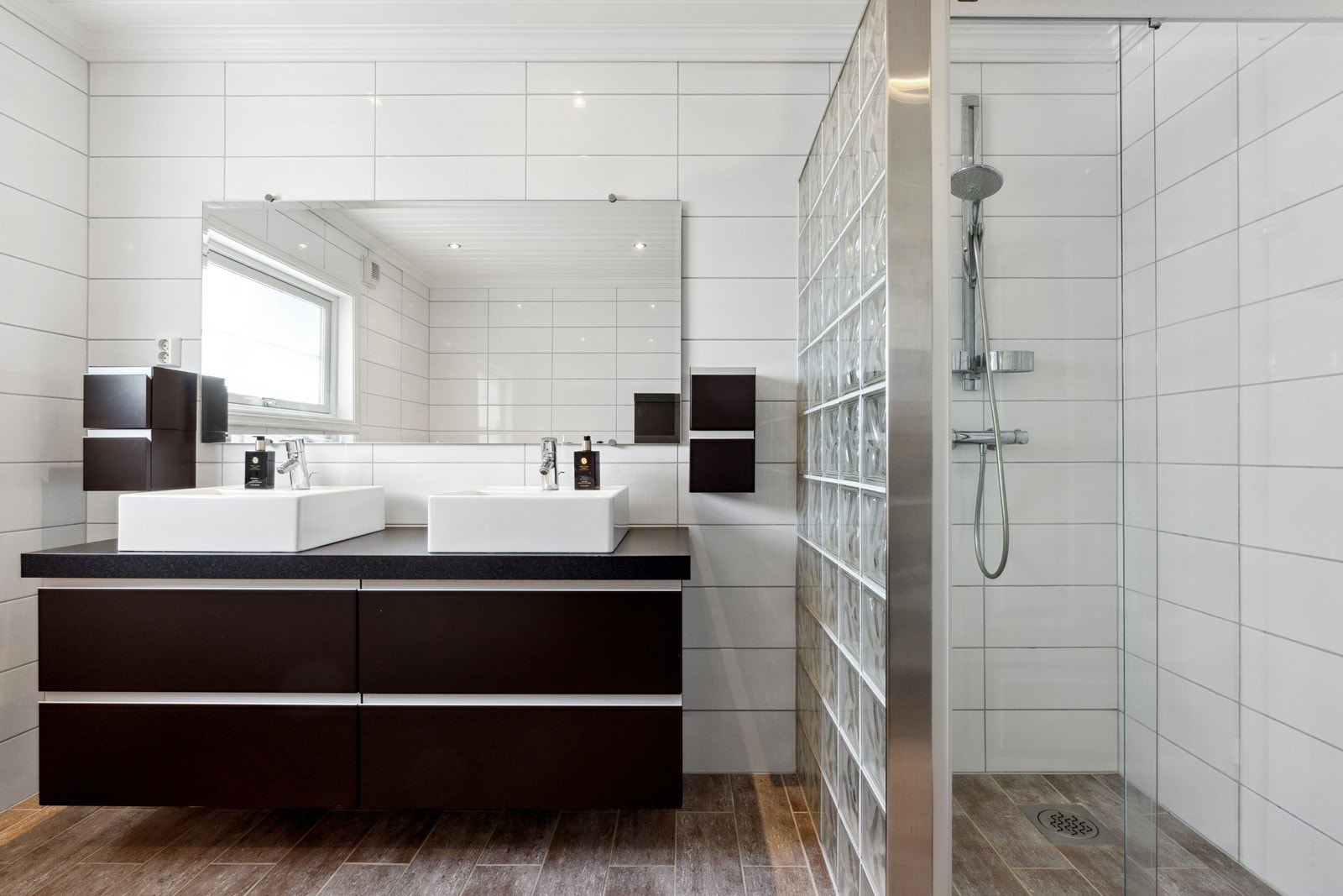 Badet er innredet med servantinnredning med skuffer og to ovenpåliggende servanter, to vegghengt skap, vegghengt toalett, hjørne-boblebadekar og dusjnisje med glassbyggesten og glassdør. Galleribilde