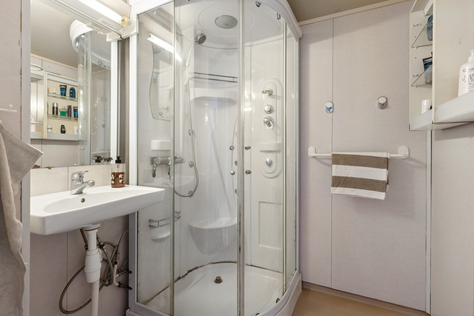 Badet har plater på vegg og belegg på gulv. Rommet er innredet med servant med underskap og dusjkabinett. Galleribilde