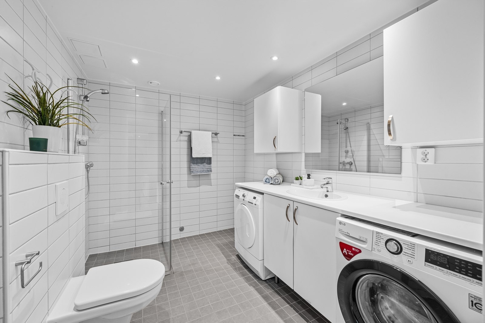 Stort og flislagt bad fra 2017 med varmekabler - Dusj på gulv med dører i herdet glass, veggfestet klosett og servant Galleribilde