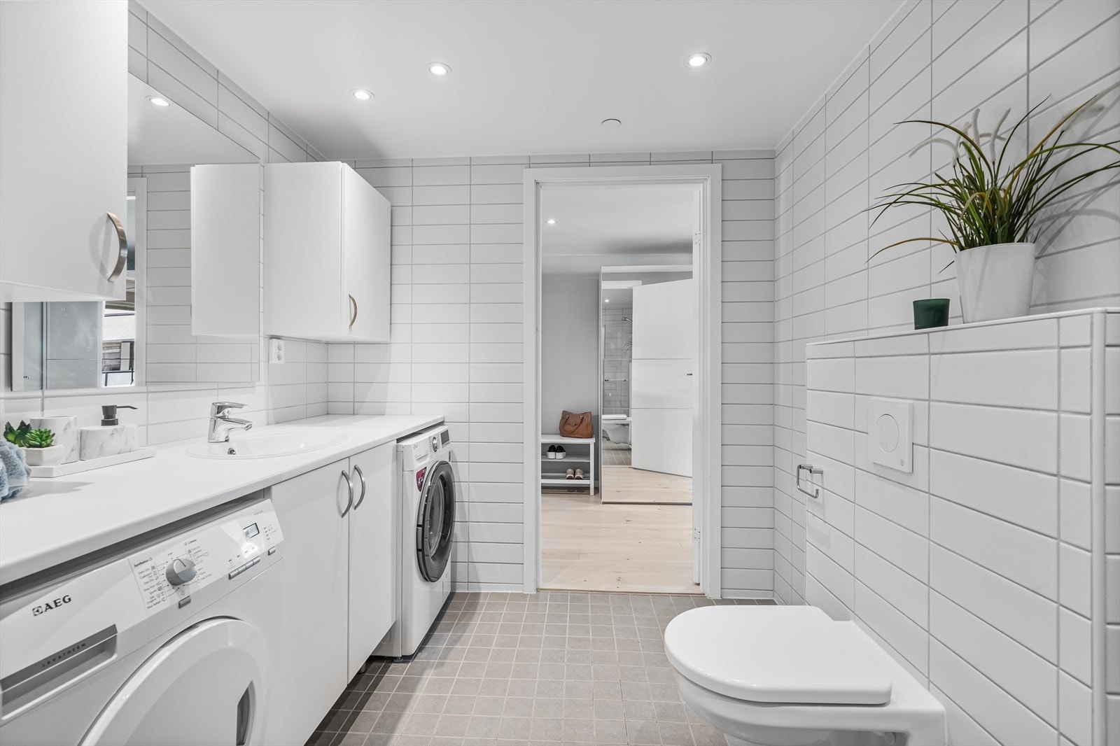 Videre er det benkeskap og overskap med glatte fronter, laminat benkeplate og speil over servant - Opplegg for vaskemaskin Galleribilde