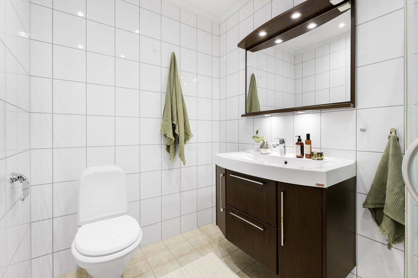 Badet i hovedetasjen inneholder toalett, helstøpt servant, skap og skuffer under servant med slette fronter, dusjdører i klart glass og opplegg for vaskemaskin Galleribilde