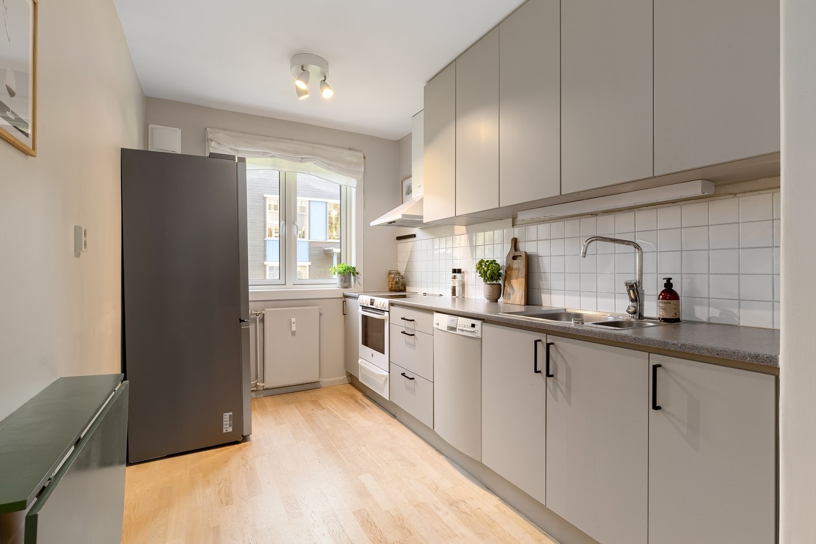 Takhøy innredning med glatte, malte fronter. Frontene ble pusset og malt i juni 2024. Laminat benkeplate med nedfelt kum i rustfritt stål. Flisfelt på vegg over benk. Galleribilde