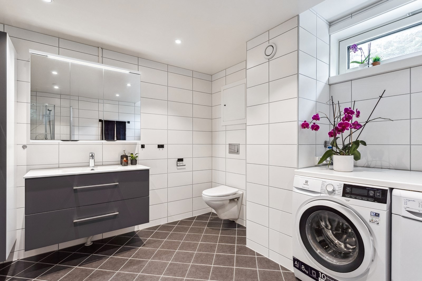 Rommet er av særdeles god størrelse, og er utstyrt med stort dusjhjørne, servant med praktiske oppbevaringsløsninger, vegghengt toalett og opplegg for både vaskemaskin og tørketrommel. Perfekt for familien! Galleribilde