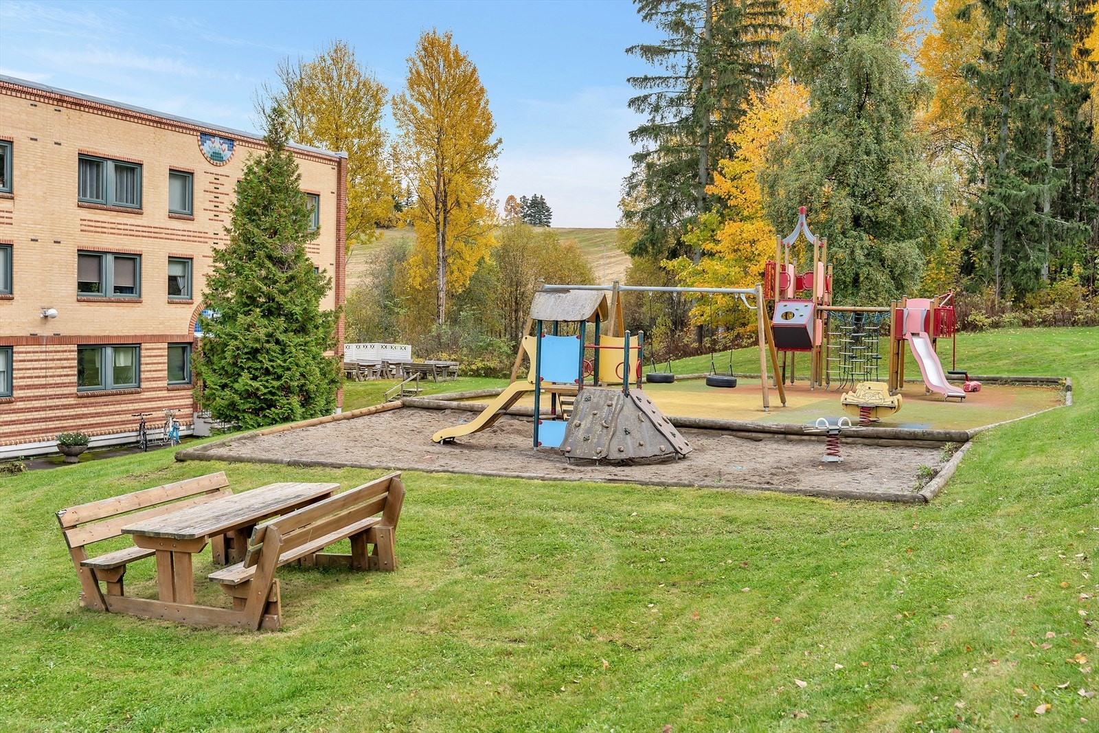 Fellestomten skråner mot øst, og er opparbeidet med lekeområder, plen og beplantning. Asfalterte internveier og biloppstillingsplasser. Galleribilde