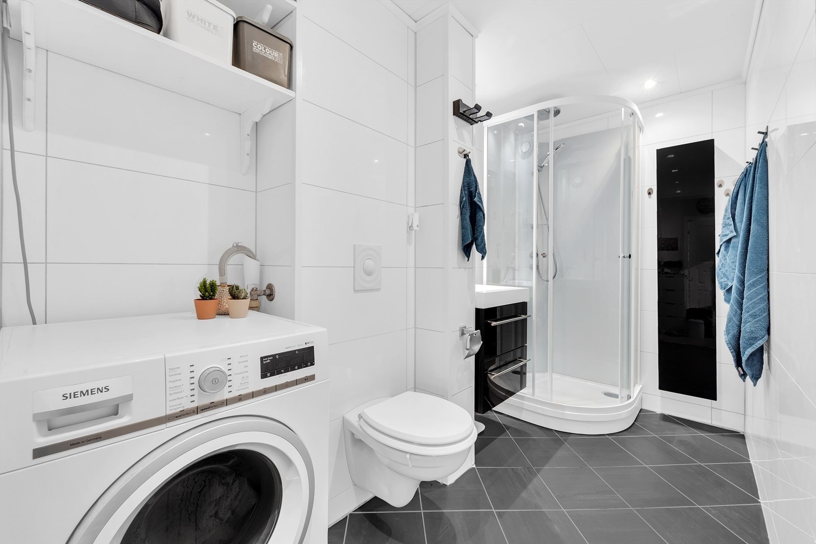 Flislagt bad fra 2009 med varmekabler i gulv og downlights i tak. Sort baderomsinnredning med servant på underskap og speil med belysning over. Ellers installasjoner med vegghengt toalett, dusjkabinett og opplegg for vaskemaskin. Galleribilde