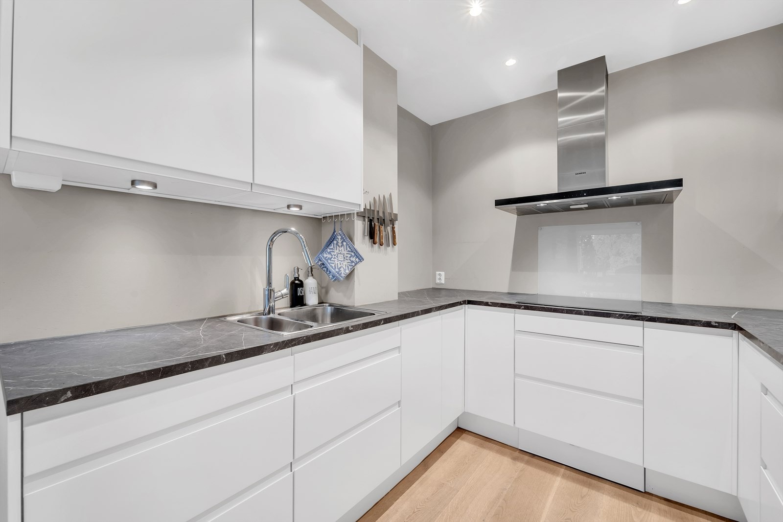 Innredningen har glatte fronter og laminert benkeplate, samt platekledning på vegg over benkeskap som tåler matlaging og vannsøl. Det er belysning under overskapene som gir godt med lys til matlagingen. Galleribilde