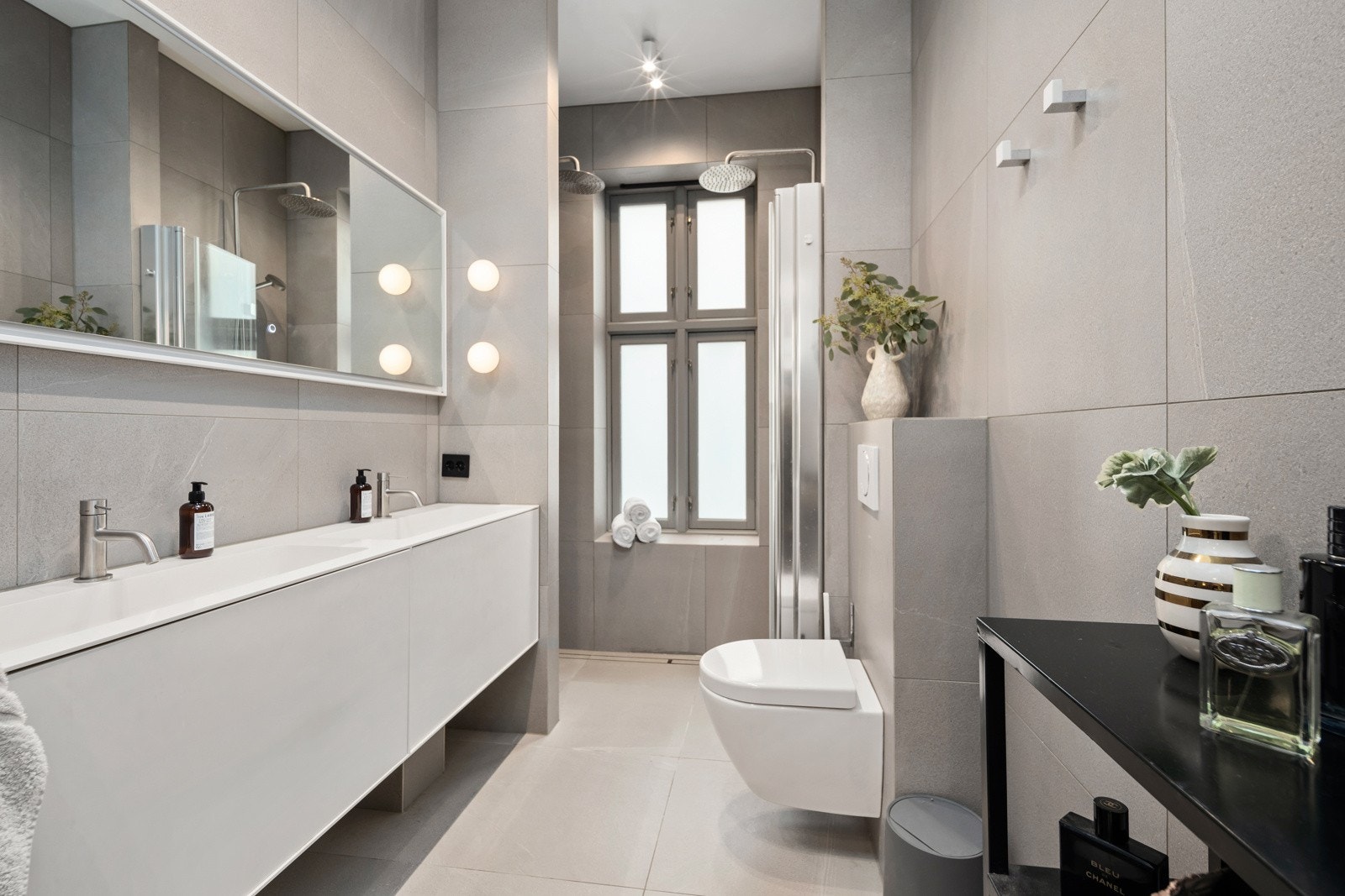 Lyst og delikat, flislagt baderom innredet med dobbel servant med servantskap, vegghengt klosett og duskjinsje. Galleribilde