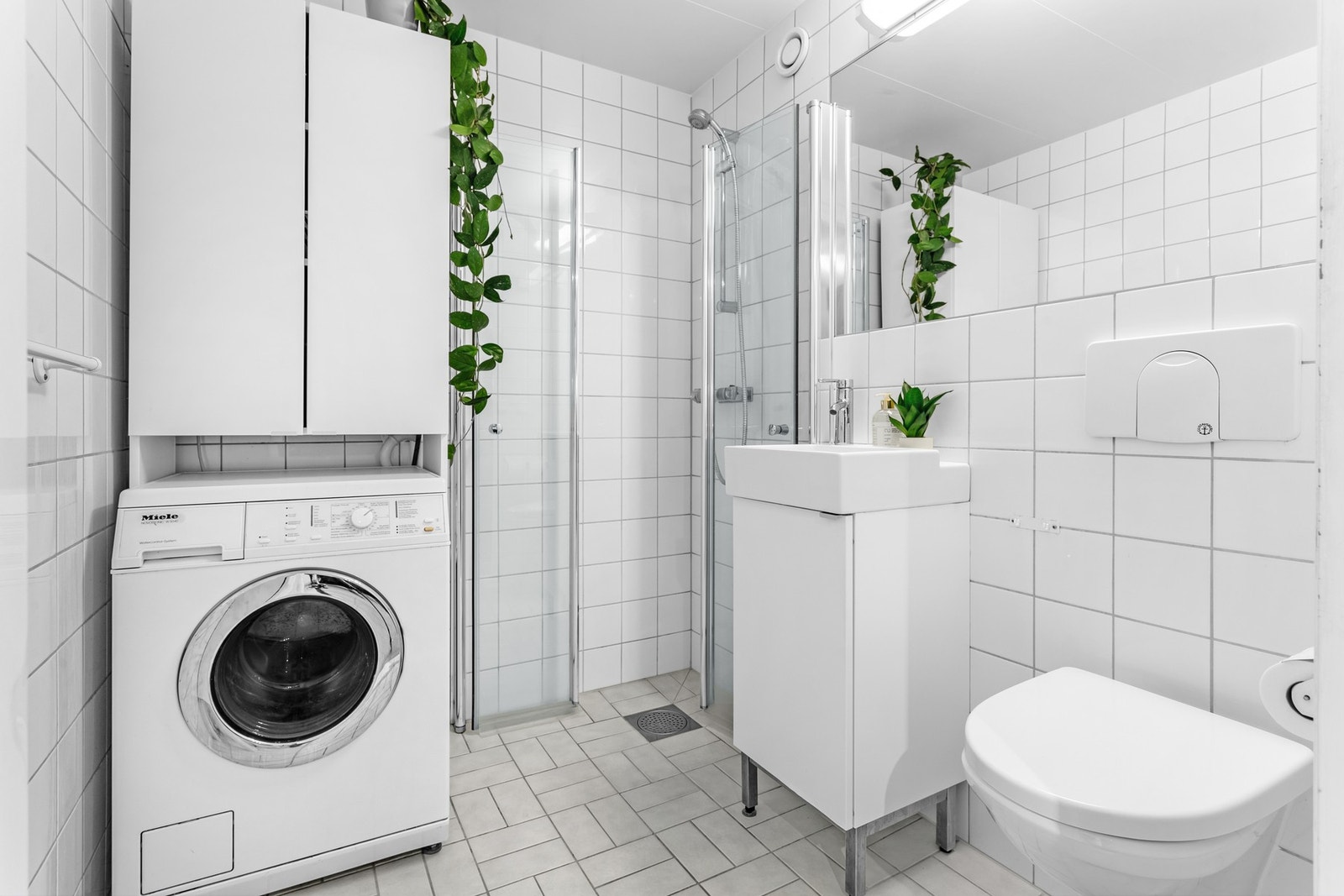 Badet inneholder servantskap med glatte fronter, veggmontert toalett og opplegg for vaskemaskin. Galleribilde