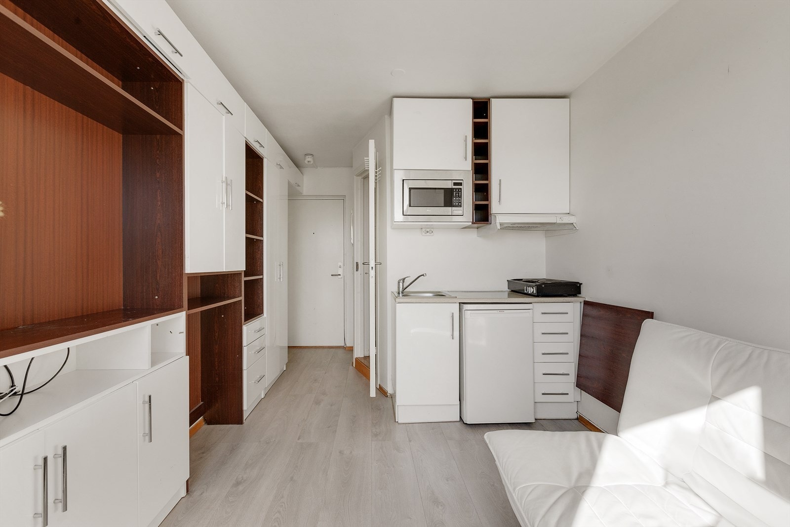 Hybelkjøkken med glatte fronter og laminert benkeplate. Kjøkkenet har frittstående kjøleskap og mikrobølgeovn, samt ventilator med mulighet for løs platetopp under. Galleribilde