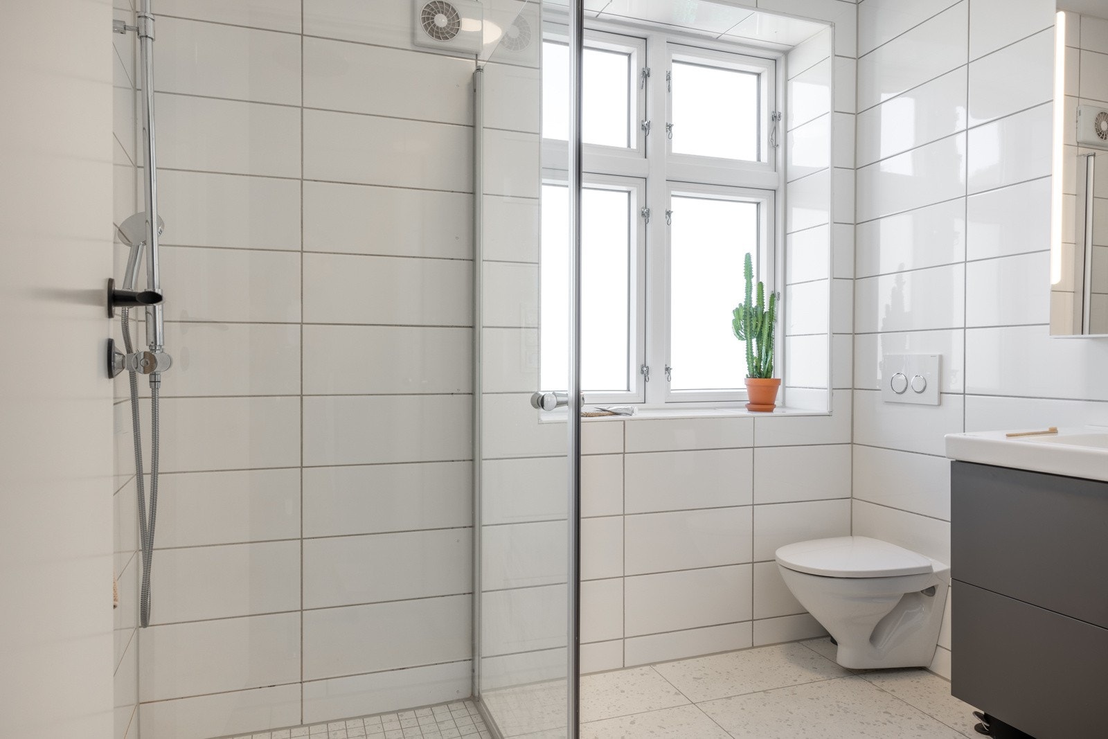 Badet er av god størrelse på 4,2kvm og inneholder et vegghengt toalett, dusjhjørne med glassdører, rør-i-rør fordelerskap og baderomsinnredning med heldekkende servant, speil og belysning. Galleribilde