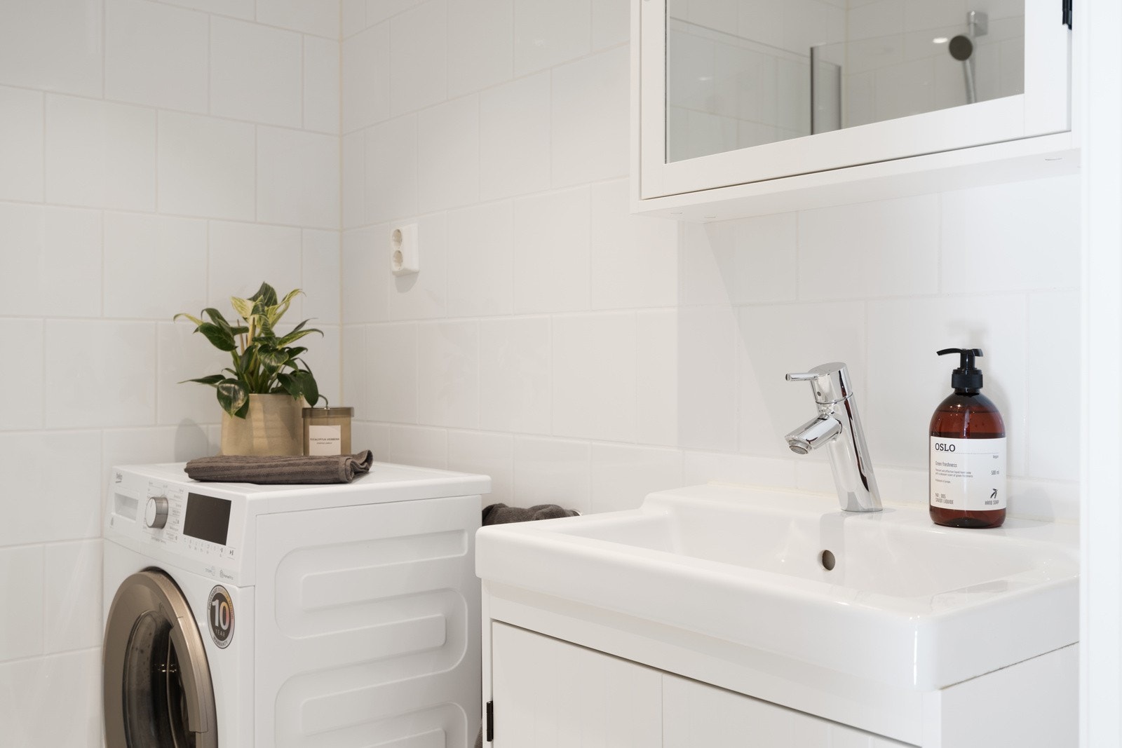 Rommet er videre utstyrt med en lys baderomsinnredning, supplert med speilskap, toalett, dusjhjørne med innfellbare glassdører og opplegg for vaskemaskin. Galleribilde