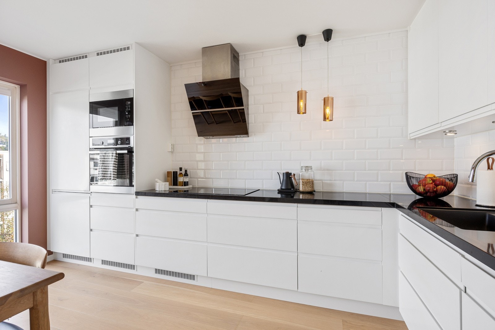 Kjøkkenet har takhøye skap, hvite, glatte fronter med gripekant og en påkostet benkeplate i sort steinkompositt. Galleribilde