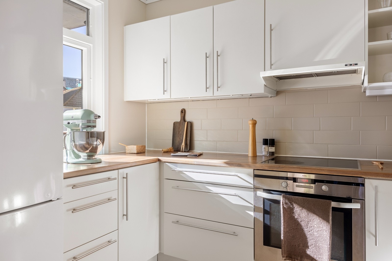 Stilren kjøkkeninnredning med hvite, slette fronter og benkeplate i heltre. Praktisk med vindu ut mot balkongen. Galleribilde