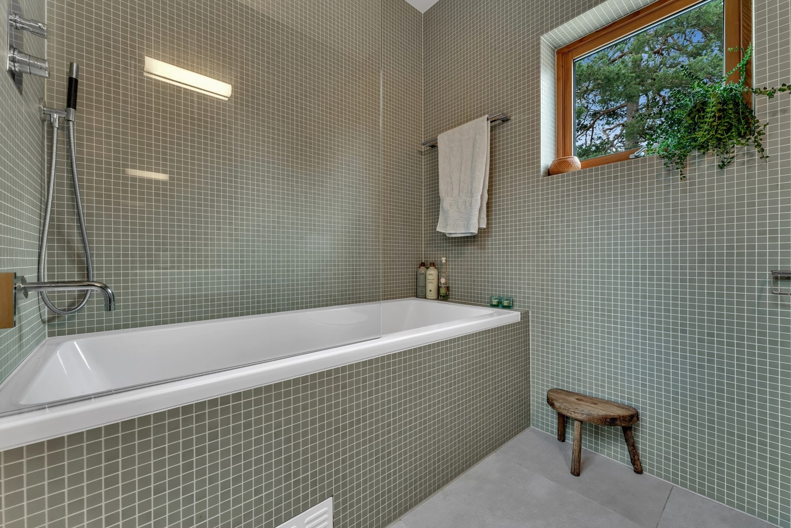 Rommet har små mosaikkfliser på vegger og store fliser på gulv Galleribilde