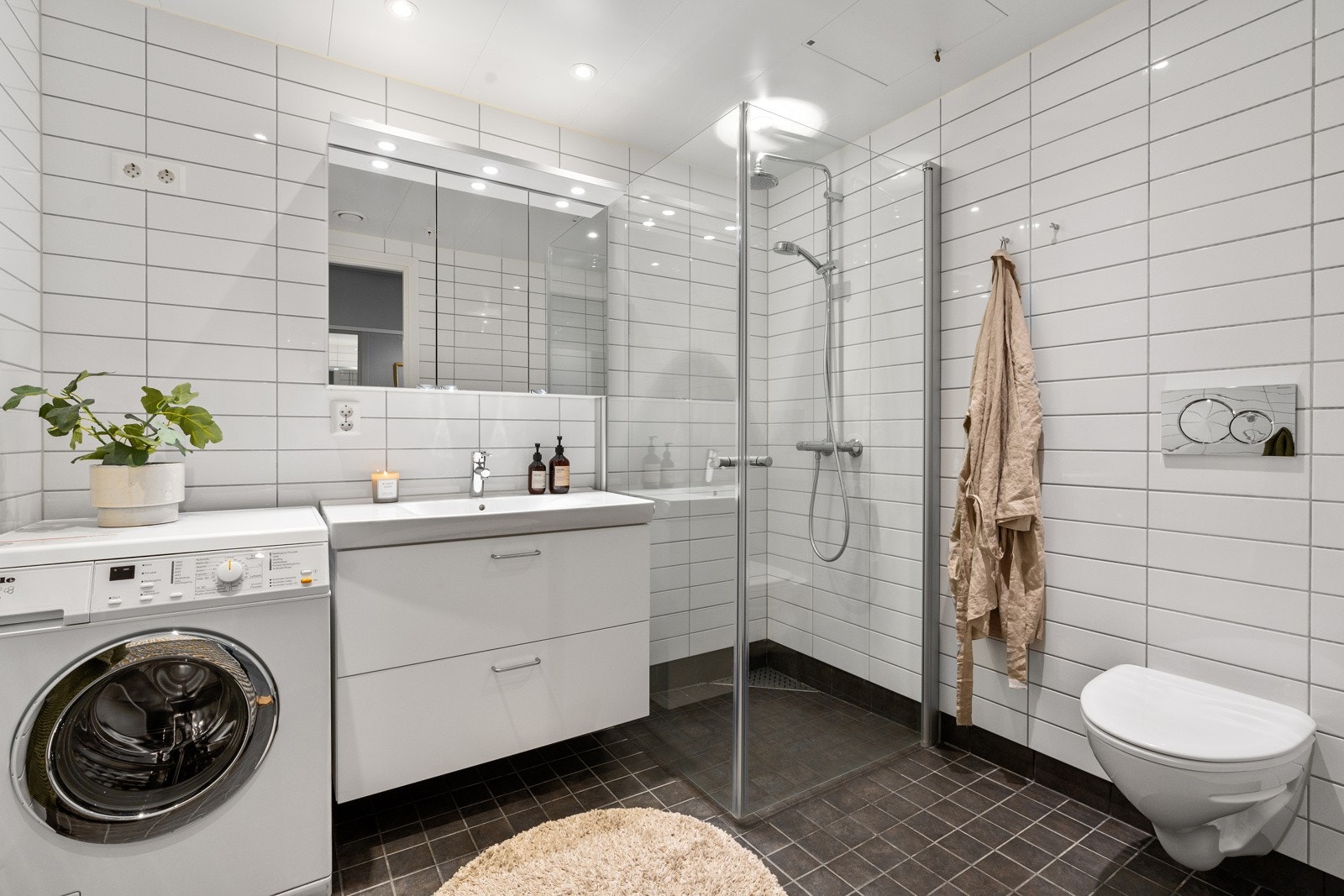 Lekkert flislagt og romslig bad med stort dusjhjørne med regndusj og praktisk vegghengt toalett. Plass til vaskemaskin og tørketrommel. Galleribilde