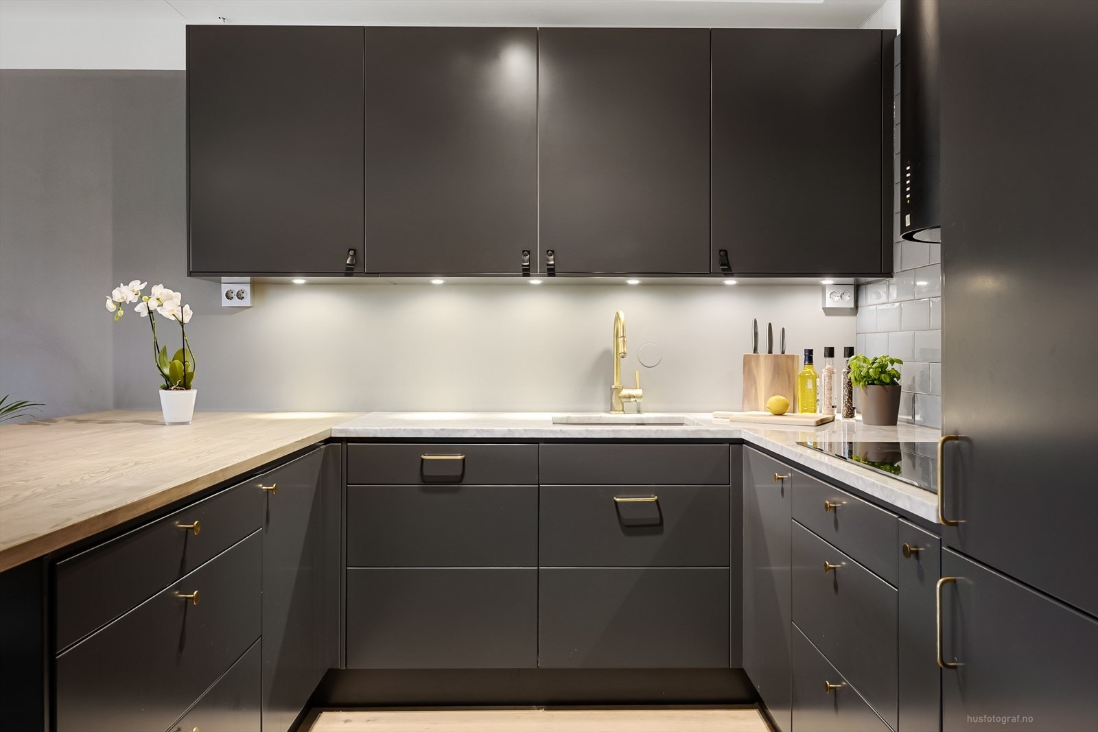 Moderne slett vegg over benkeplaten og flissatt med tidsriktige fliser over kokesonen, det er belysning under overskap. Galleribilde