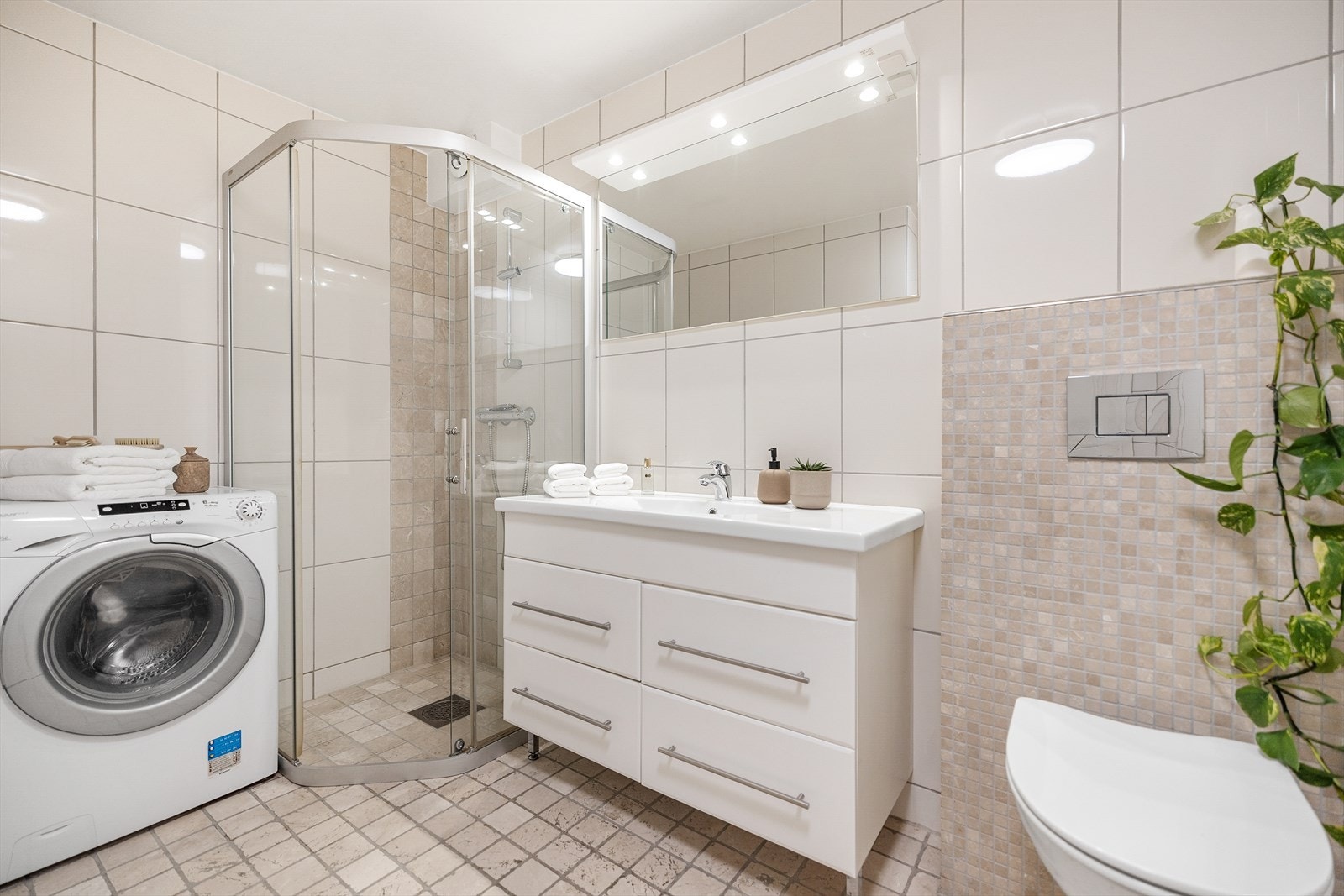 Moderne, flislagt bad med varmekabler i gulv og innredning bestående av vegghengt wc, dusjhjørne med skyvedører, samt servant i hvit skuffeseksjon med speil og belysning over. Plass og opplegg for vaskemaskin, Galleribilde