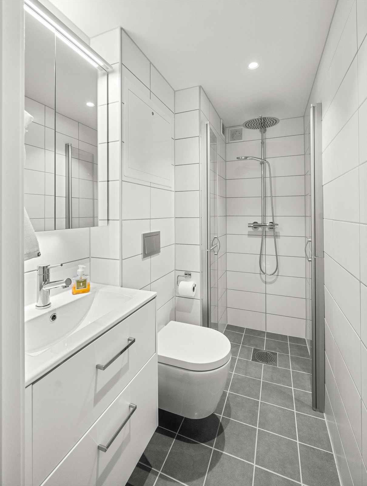 Baderom fra 2023 med flislagte vegger og malt i himling. Servant med ett-greps blandebatteri og det er opplegg for vaskemaskin. Galleribilde