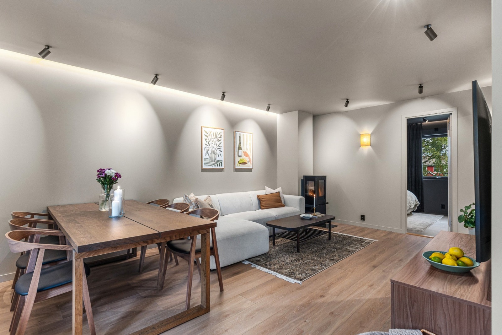 Videre kommer du raskt inn i den flotte stuen som måler 23,5 kvm. Her er det spotbelysning supplert med stilige vegglamper og innlektet ledstripe mot veggen. Godt med plass til både stort middagsbord og sofakrok. Galleribilde