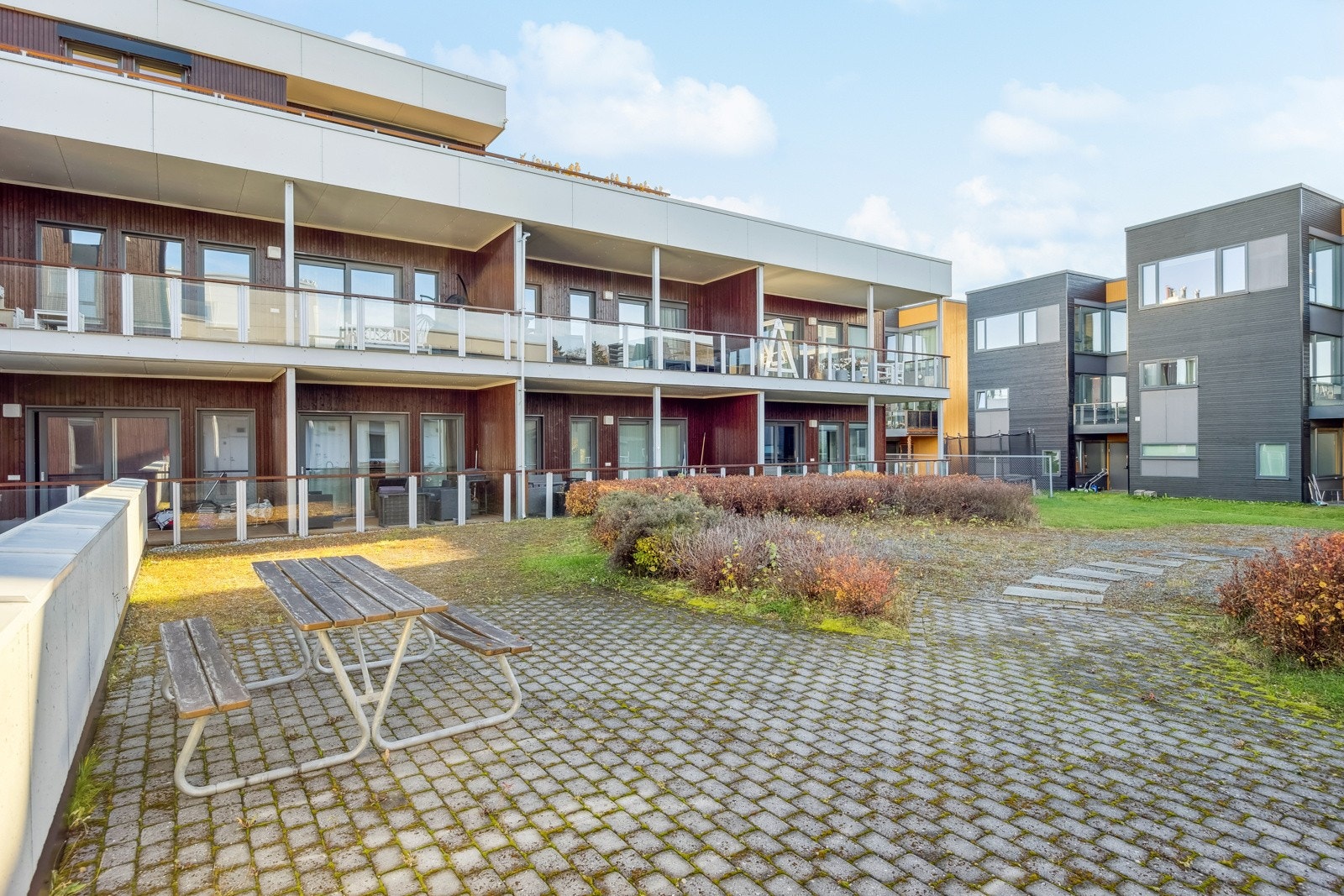 Felles tomt for sameiet opparbeidet med asfaltert vei, belegningsstein, beplantninger, biloppstillingsplass, sittegrupper og plenareal. Galleribilde