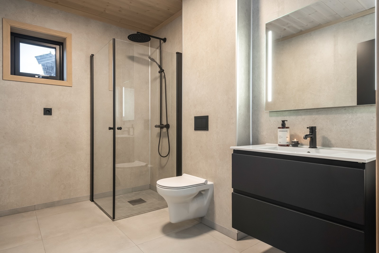 Delikat bad med 60x60 cm flis på gulv med gulvvarme og baderomsplater begge i gråtoner, i himlingen er det panel malt i hvit som komplementerer og lyser opp baderommet Galleribilde