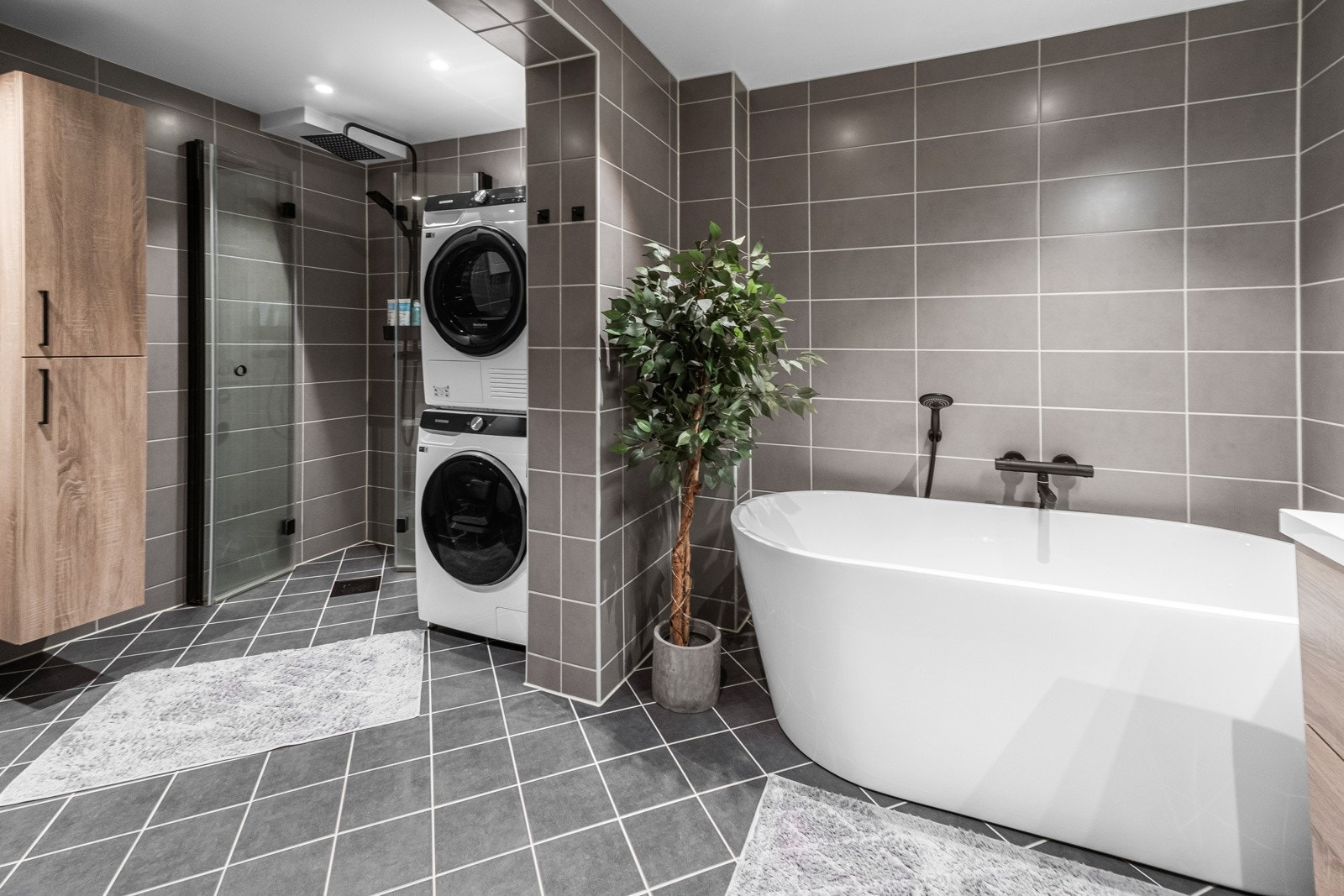 Badet kombinerer funksjonalitet med stil. Med fliser på gulv og vegger skapes et tidløst uttrykk. Innredningen inkluderer veggmontert klosett, servant med oppbevaring, og en romslig dusjnisje med elegante glassdører. Galleribilde