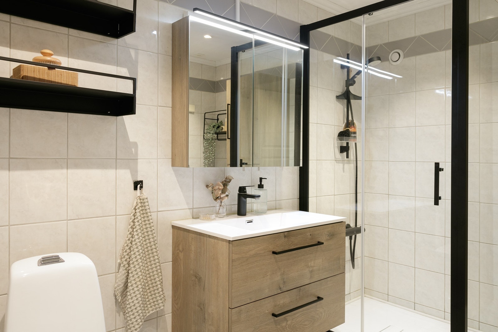 Badet er godt utstyrt med opplegg for vaskemaskin, mekanisk avtrekk og et gulvstående toalett. Dusjhjørnet er avgrenset med stilrene glassvegger og har dusjgarnityr samt dusjkar Galleribilde