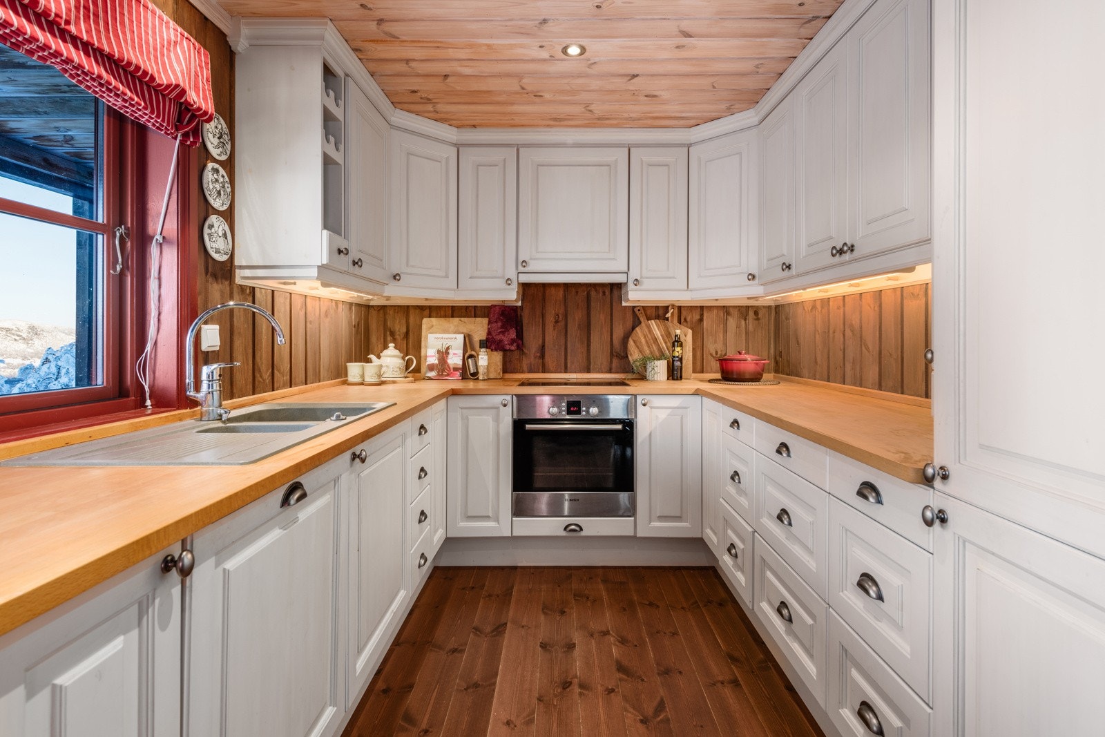 Innredningen er malt i en klassisk hvitfarge med håndtak i stål. Benkeplatene er i heltre. Alle hvitevarene er integrert i innredningen. Galleribilde