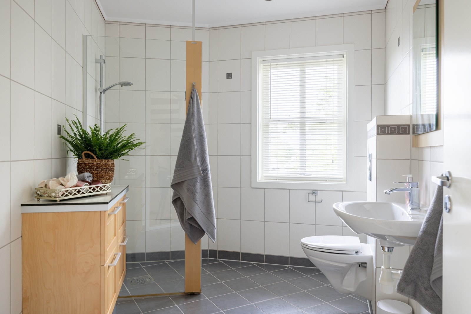 I boligens 1. etasje har du et lyst og tidløst flislagt baderom fra byggeåret 2002. Baderommet har grå fliser på gulv med gulvvarme, hvite fliser på veggene. downlights i himlingen og balansert ventilasjon. Galleribilde