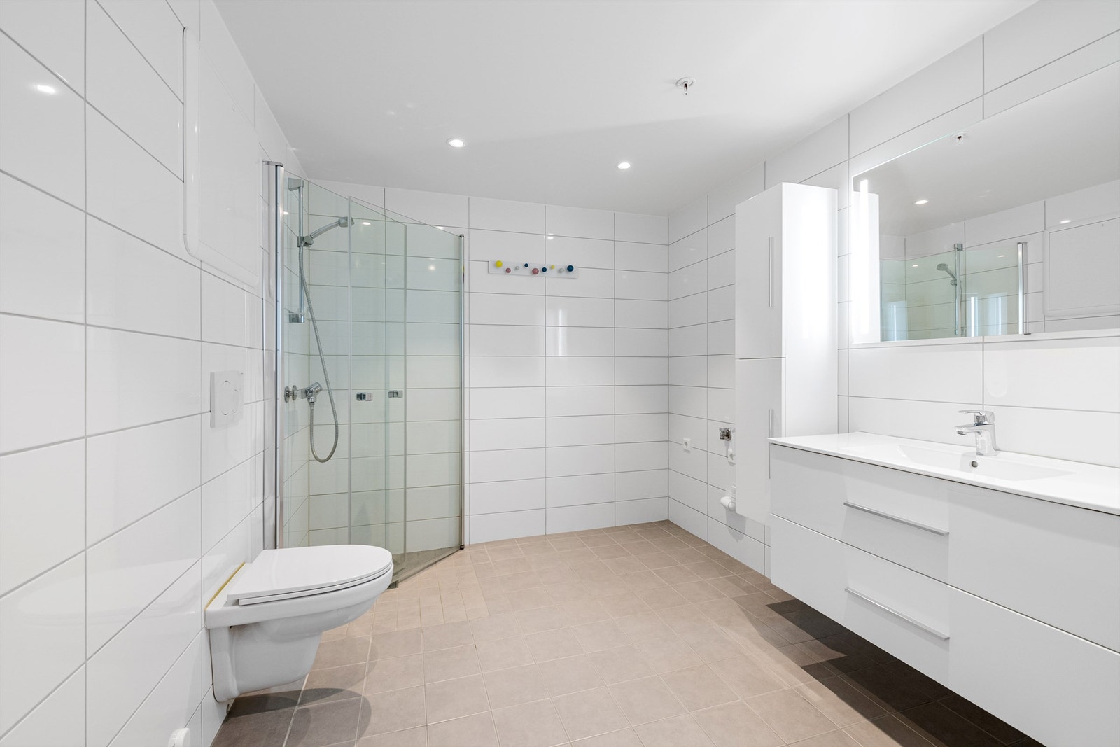 Stort romslig og flislagt bad.
Dusjhørne med dører og vegghengt dusjarmatur. Vegghengt toalett. Opplegg for vaskemaskin. Galleribilde