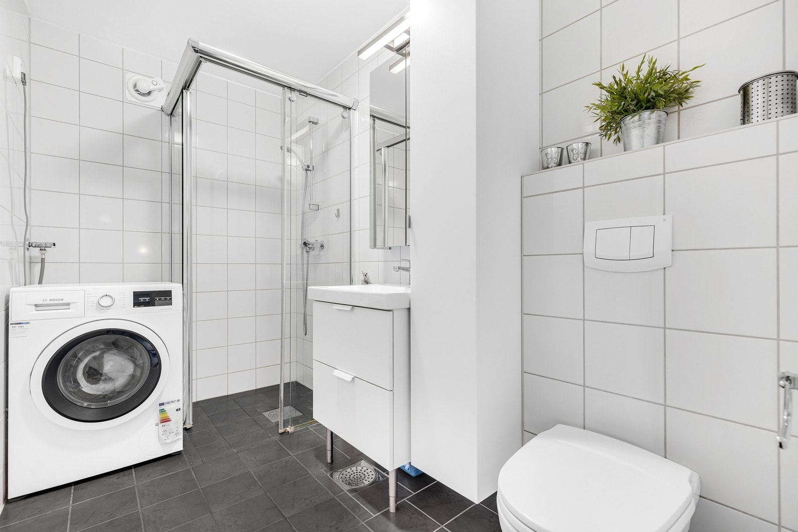 Pent flislagt bad på 4,4m² med moderne innredning og en romslig dusjnisje. Opplegg for vaskemaskin. Galleribilde