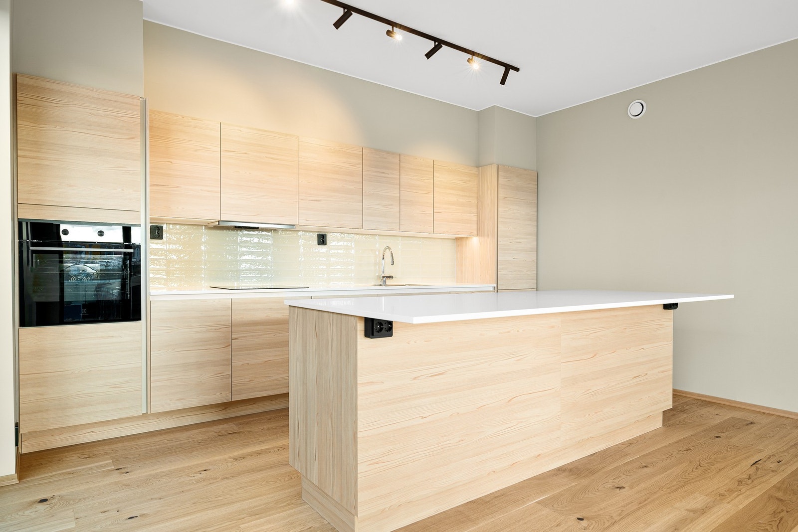 Rålekkert kjøkken i lyst tre som i kombinasjon med den hvite benkeplaten og flisene mellom under- og overskap, sørger for et gjennomført uttrykk. Galleribilde