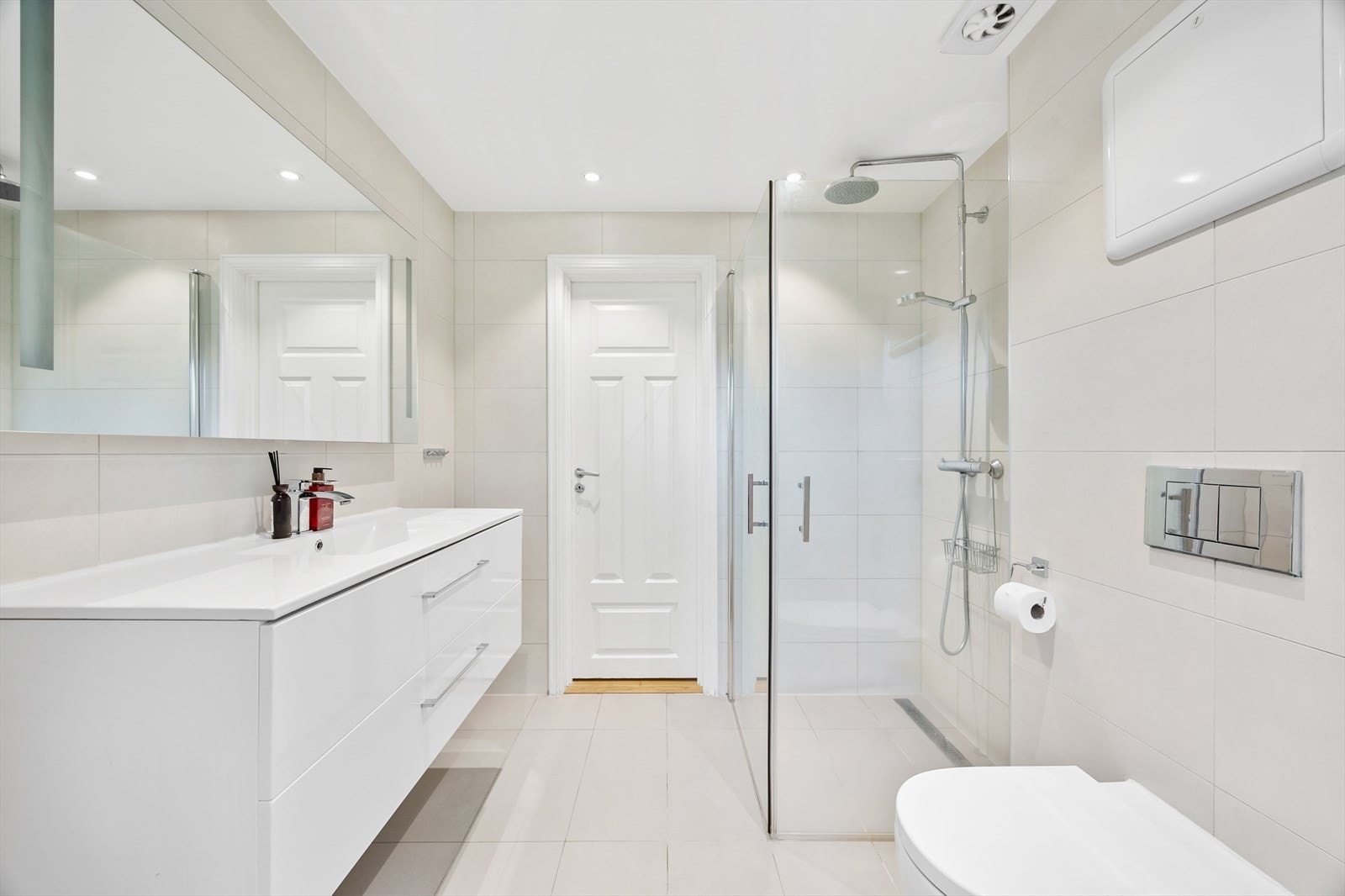 Badet er utstyrt med dusjhjørne med innfellbare glassvegger, vegghengt wc og servantinnredning med skuffer Galleribilde