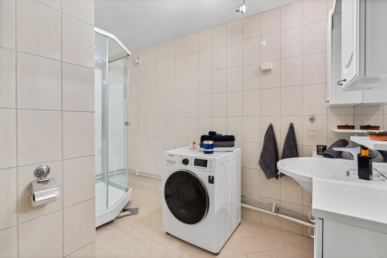 Badet har opplegg for vaskemaskin, dusjkabinett med skyvedør av glass og dusjarmatur tilkoblet hånd- og regndusj og frittstående toalett. Galleribilde