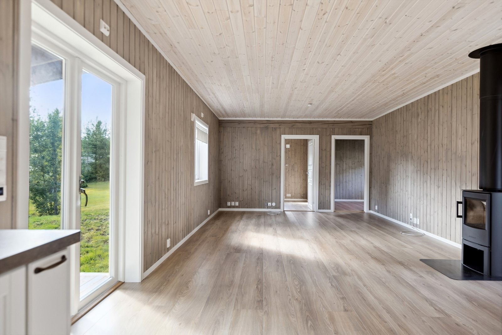 Lys og trivelig stue med beiset trepanel på vegger, laminatgulv og behandlet trepanel i himling. Galleribilde