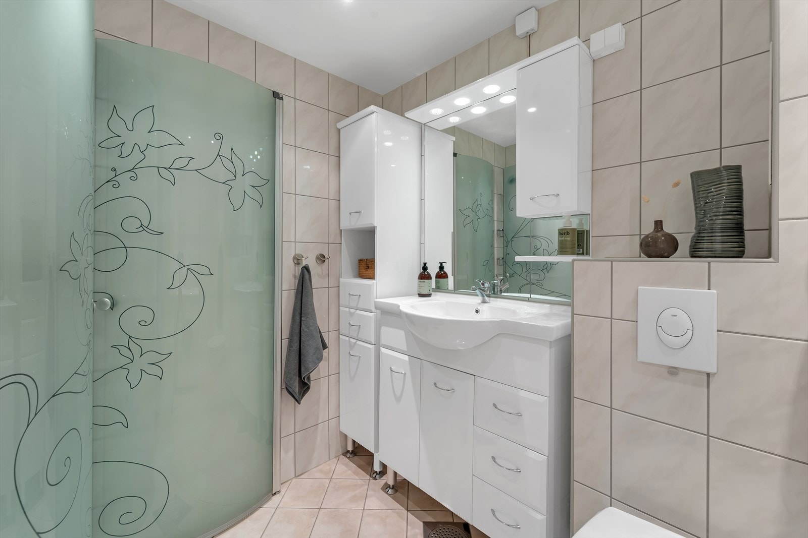 Innredningen består av vegghengt wc, hengslede dusjdører, servant med underskuffer, veggskap, høyskap, speil med overlys, opplegg for vaskemaskin og elektriske varmekabler i gulv. Galleribilde