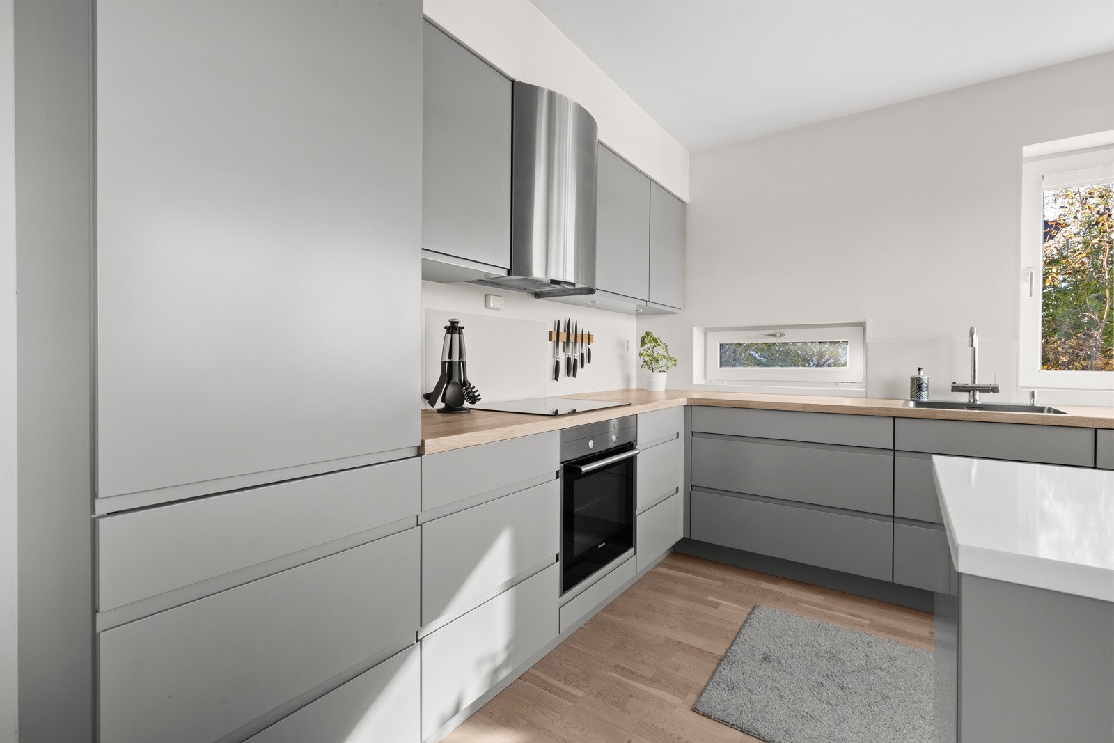 Kjøkkeninnredning med malte fronter, kompositt- og heltre eik benkeplate, glassplater over steketopp og oppvaskkum Galleribilde