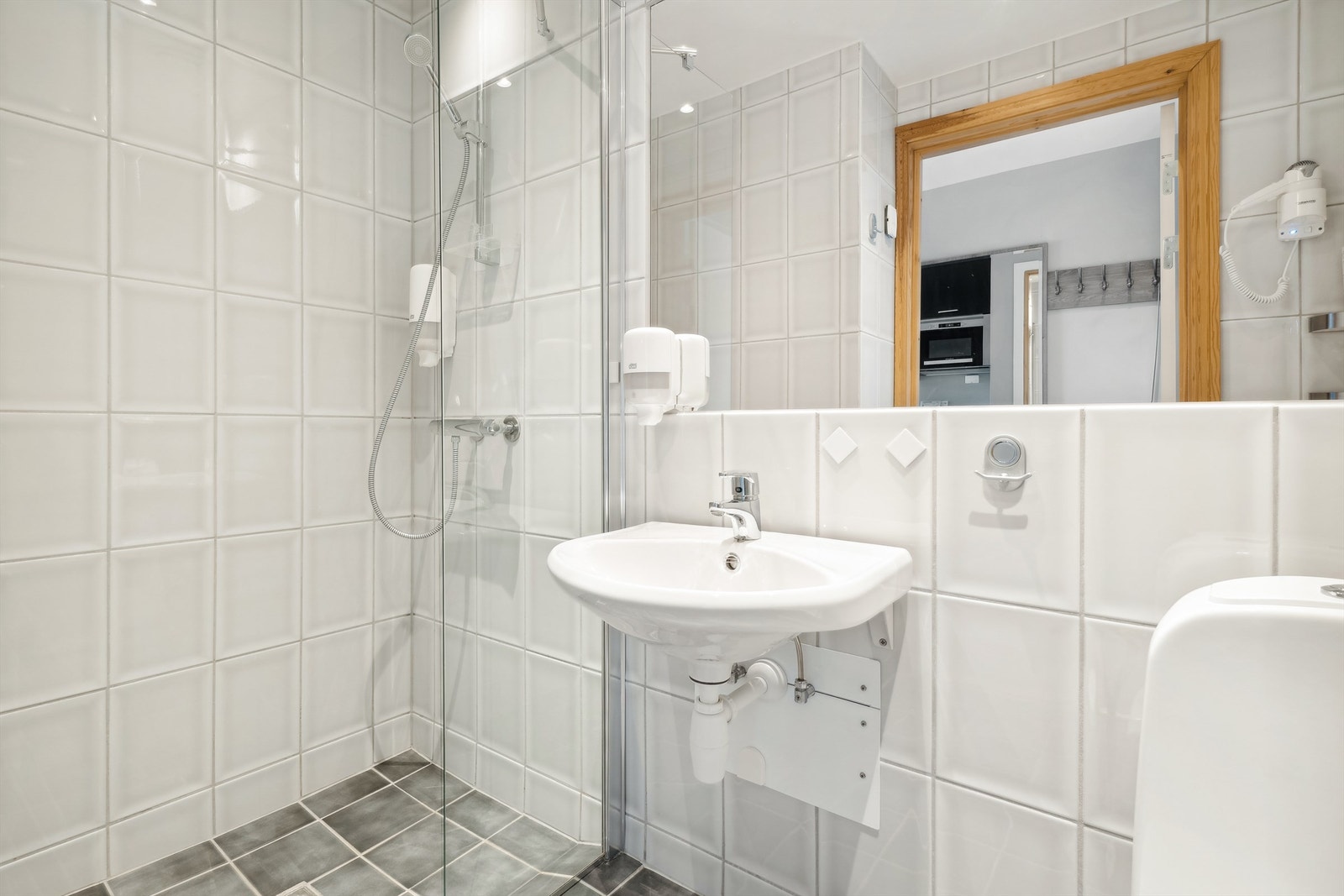 Innredet med dusjnisje med veggmontert dusjarmatur med glassvegger. Vegghengt servant og speil. Galleribilde