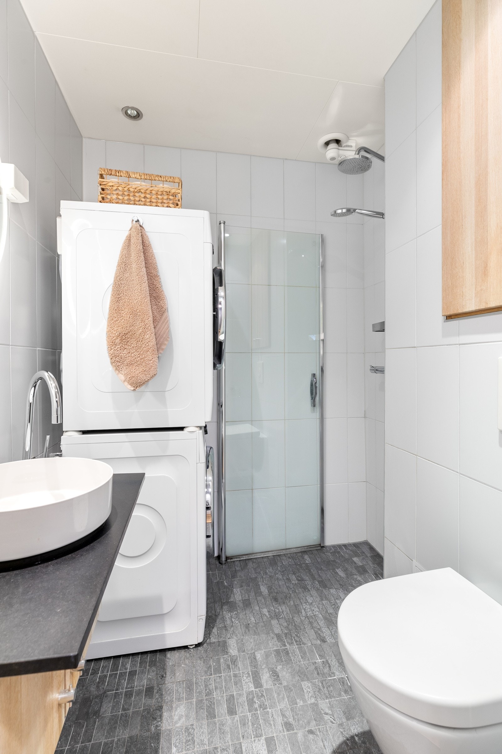 Flislagt bad med varmekabler, dusjhjørne, veggmontert servantinnredning og toalett samt opplegg for vaskemaskin Galleribilde