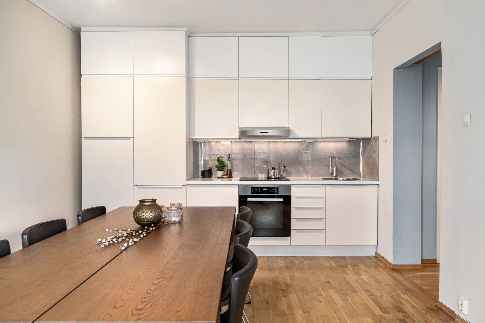 Kjøkkeninnredning med slette fronter, stålgrep, overskap med benkebelysning og fliser på vegger Galleribilde