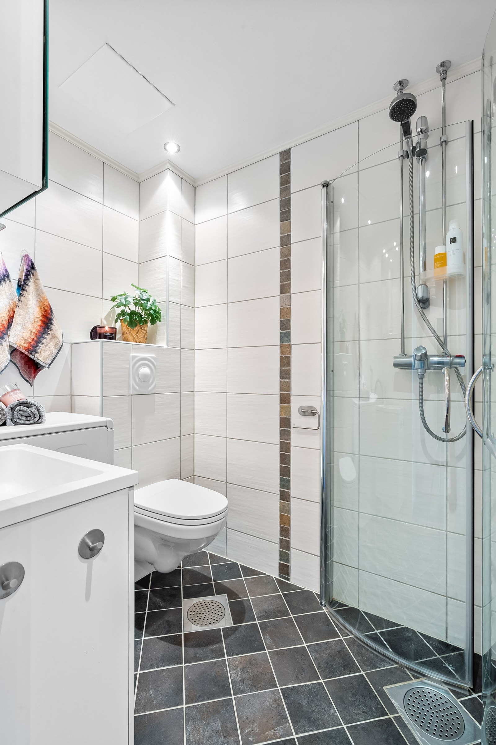 Badet er flislagt, har termostatstyrte varmekabler og downlights i himling. Badet har veggmontert toalett og dusjsone med svingdører i glass. Galleribilde