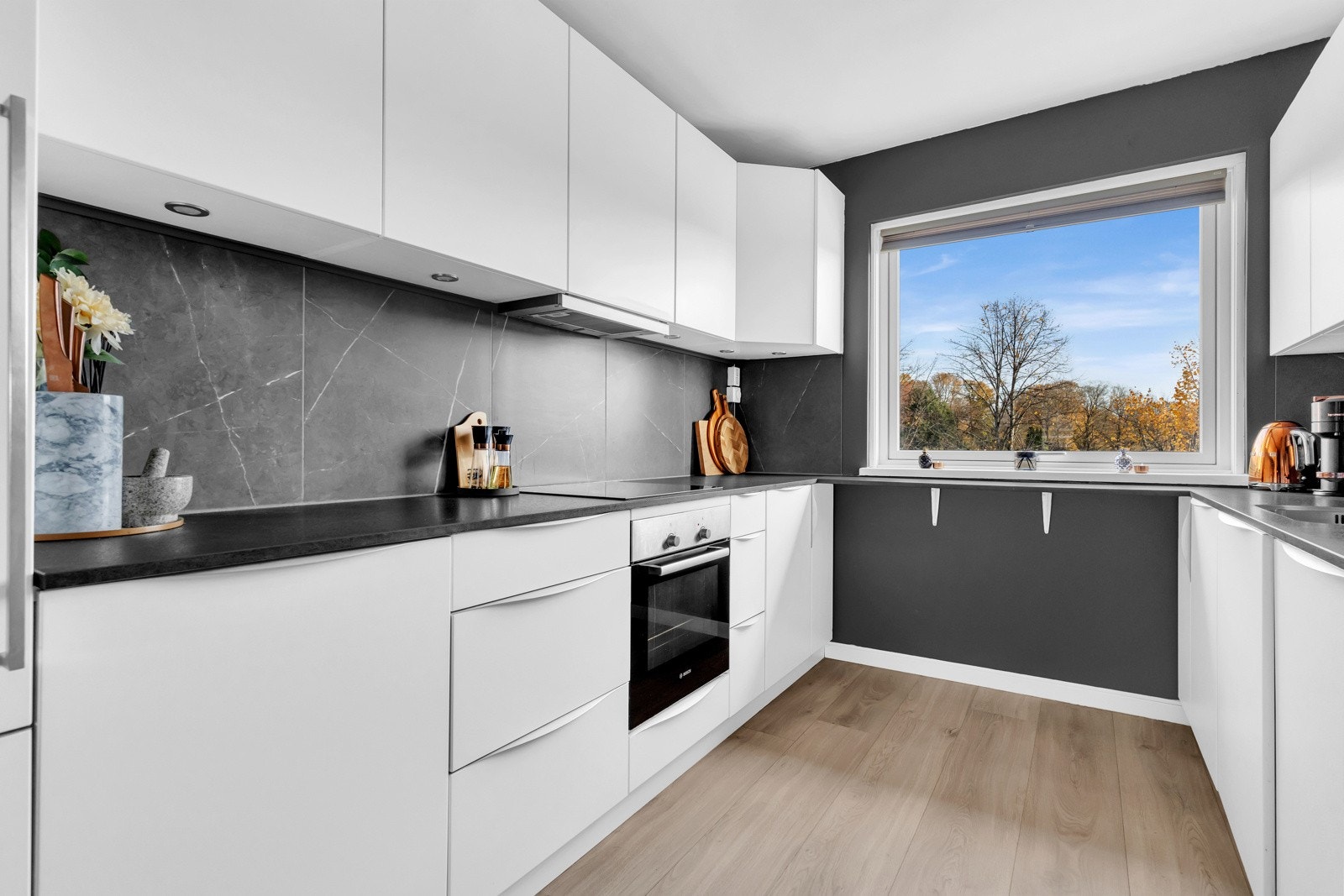 Innredningen har glatte, hvite fronter og laminat benkeplater med tilhørende veggplater mellom overskap og benk Galleribilde