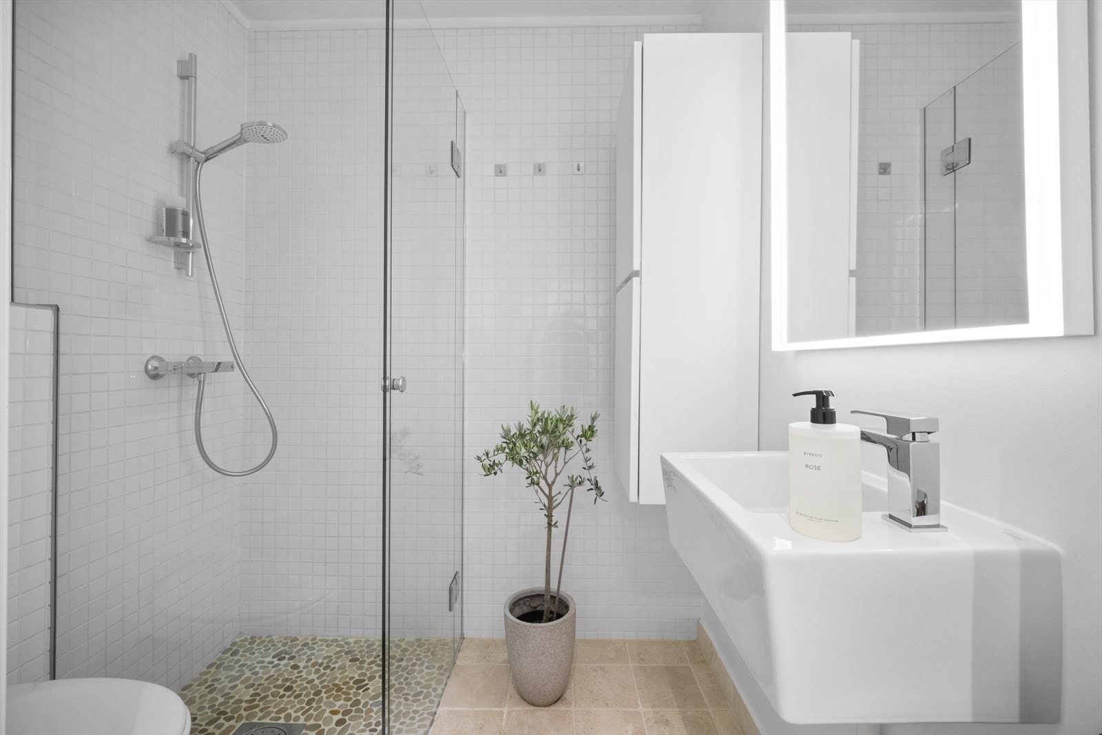 Bad med servant, veggfestet toalett, hjørnedusj med innsvingbare glassdører og vegghengt toalett. Galleribilde