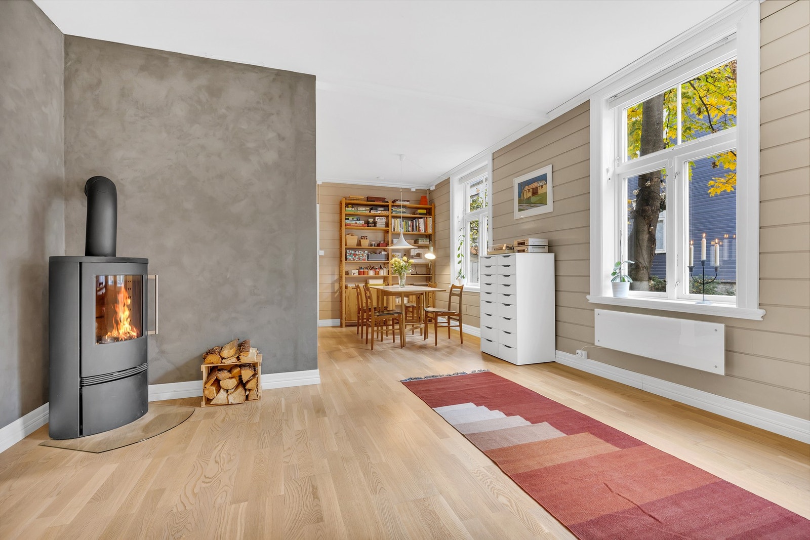 Med moderne fargevalg på vegg kombinert med store vindusposter lange hele veggen, skapes en lys og behagelig atmosfære i stuerommet. Galleribilde